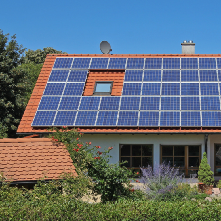 Photovoltaikanlage Haus mit rotem Dach und Solarpanelen, umgeben von Bäumen und Pflanzen.